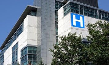 A large, modern hospital building, marked with a prominent blue 